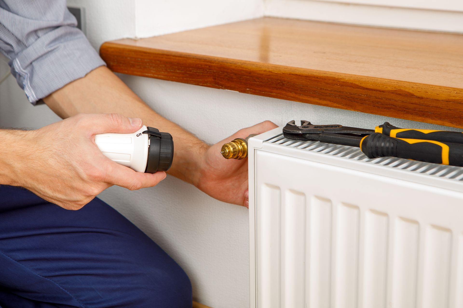 Un plombier-chauffagiste qui fixe un thermostat à un radiateur.