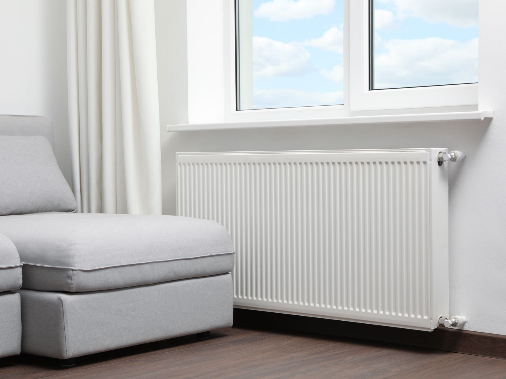 Un radiateur sous une fenêtre, à côté d'un canapé.