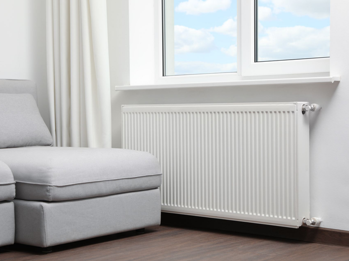 Un radiateur sous une fenêtre, à côté d'un canapé.