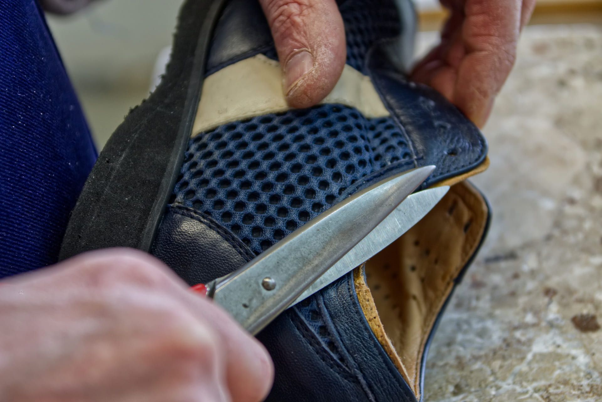 Des mains découpent une chaussure bleue avec des ciseaux sur un établi.