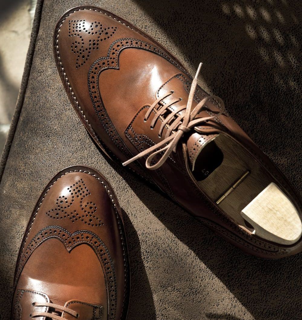 Chaussures habillées en cuir marron avec détails brogues sur une surface texturée, un lacet défait.