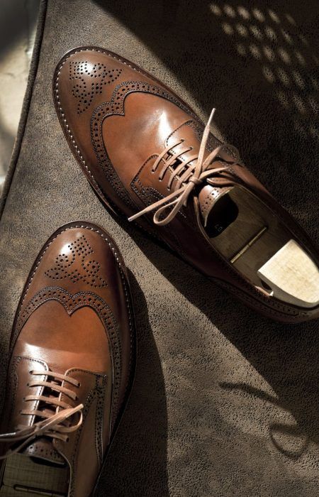Une paire de chaussures habillées en cuir marron sur un sol ensoleillé, vues de dessus.