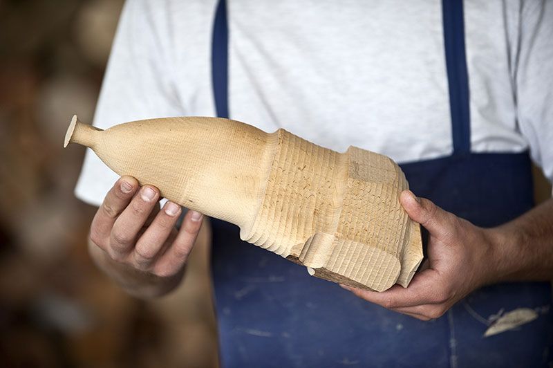 Personne tenant un objet emballé dans du papier beige dans un atelier, portant une chemise blanche et un tablier bleu