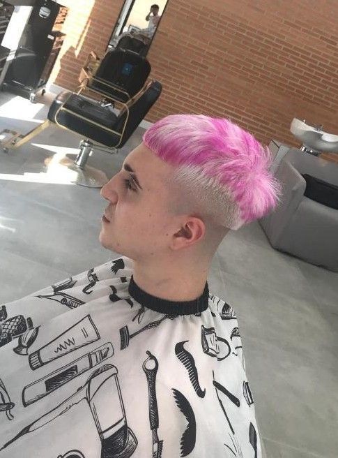 Persona con cabello rosa, cortado al rape, con capa de barbero, en un salón.