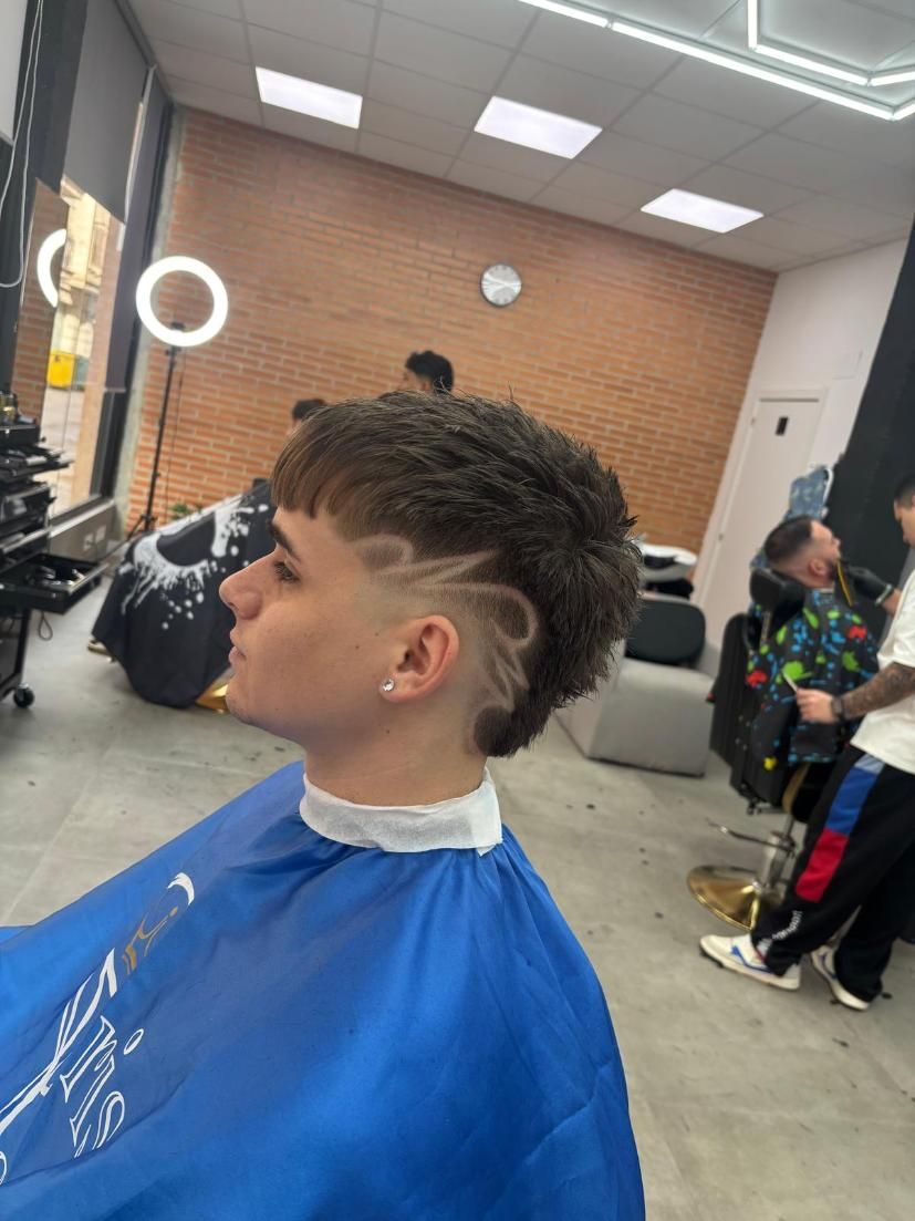 Persona con un nuevo corte de pelo en una barbería. Presenta un diseño rapado en un lateral de la cabeza. Capa azul.