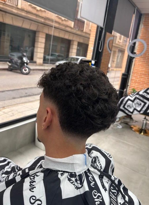 Una persona con un peinado texturizado, corte de pelo degradado hacia un lado en una barbería.