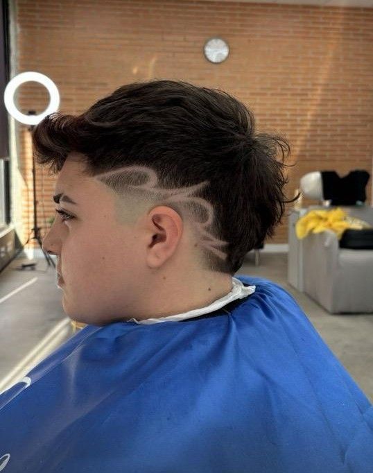 Persona con cabello oscuro texturizado y lados afeitados, diseño estampado, vistiendo una capa de barbero azul.