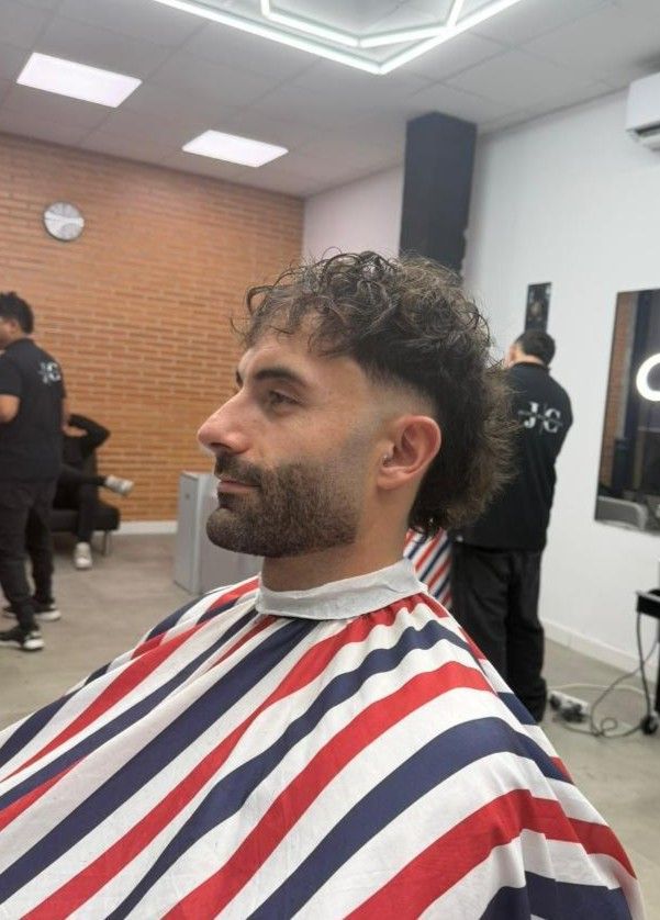 Un hombre con cabello rizado y un salmonete cortándose el pelo en una barbería.