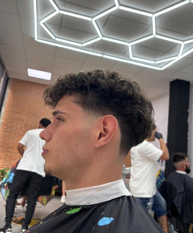 Hombre con cabello rizado y un corte de pelo descolorido en una barbería, vista lateral.