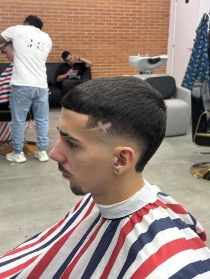 Hombre con un corte de pelo degradado y diseño en una barbería, vistiendo una capa de barbero.
