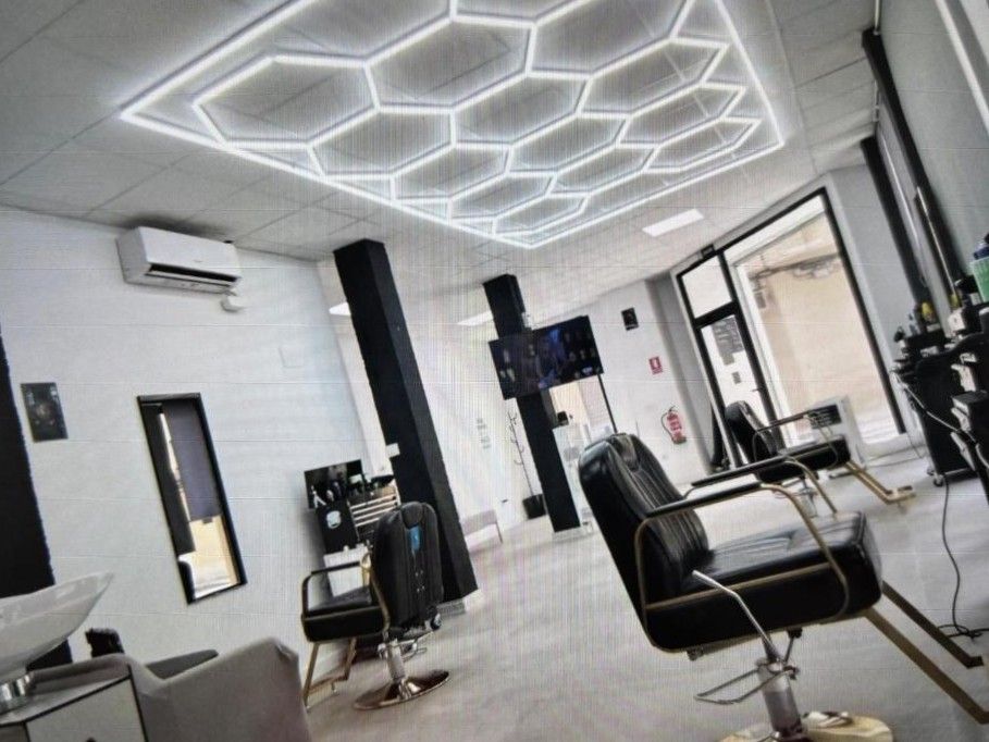 Interior de peluquería con luces de techo con diseño hexagonal, columnas y sillas negras y espejos.