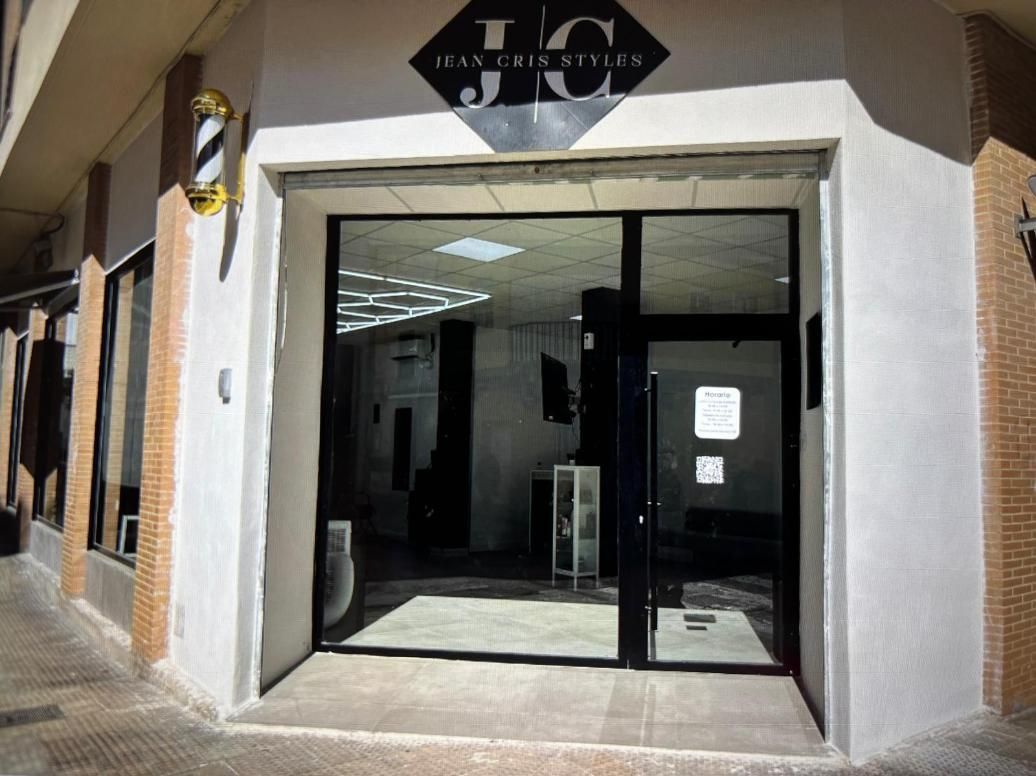 Entrada de peluquería con puertas de vidrio abiertas, molduras negras y un cartel encima.