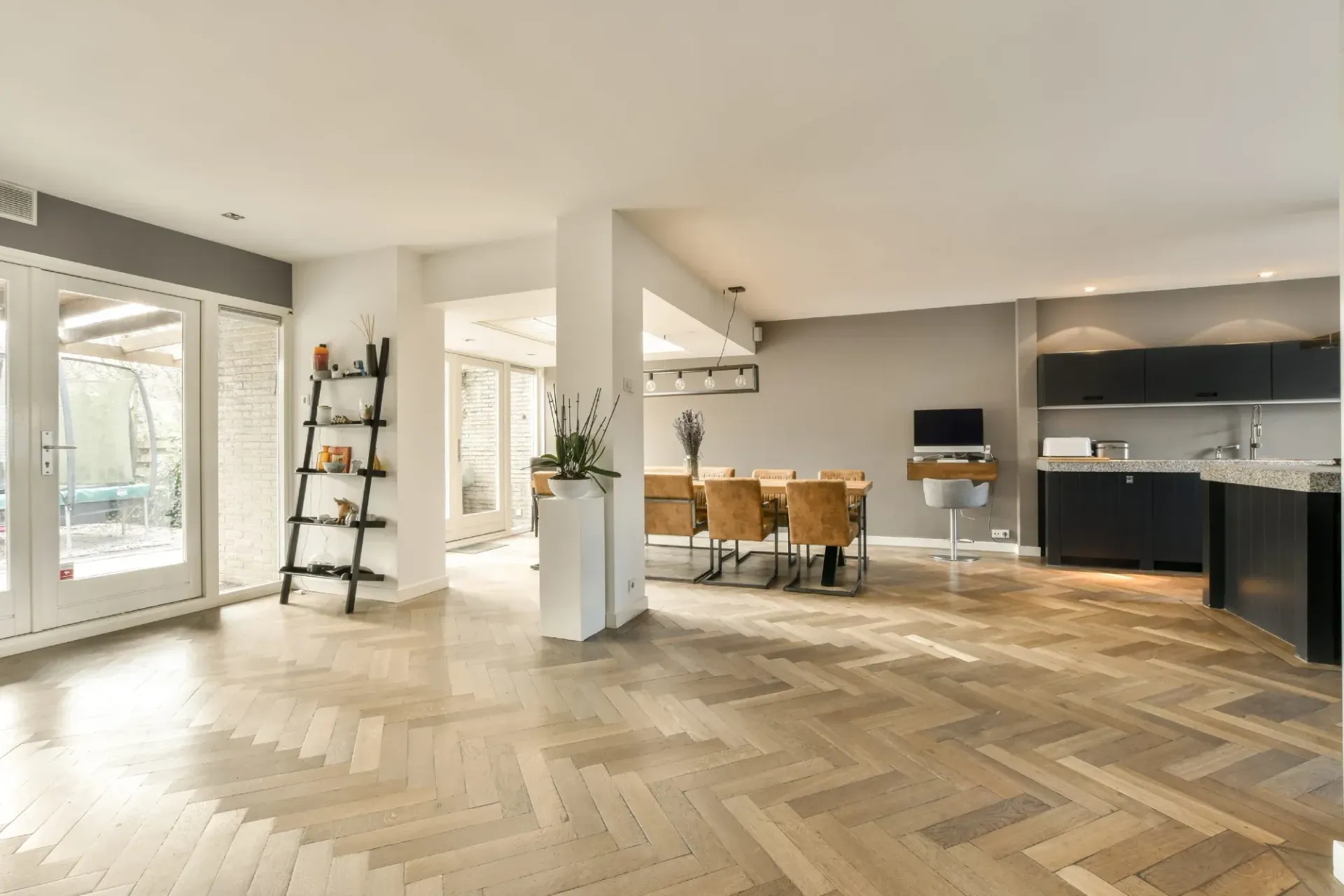 Moderna sala de estar de planta abierta con pisos de madera en espiga clara, un comedor y una cocina oscura.