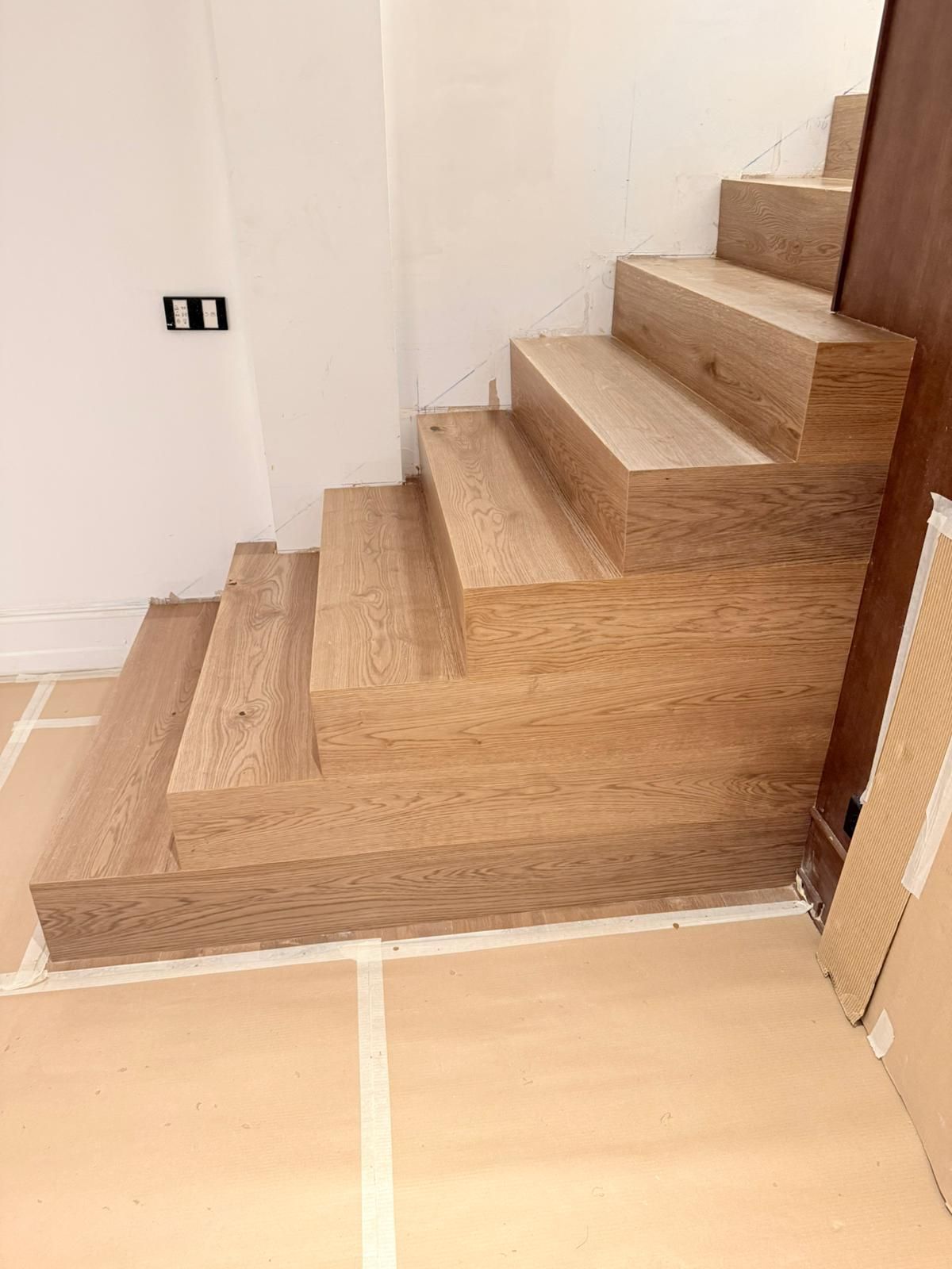 Un conjunto de escaleras de madera de color claro en construcción, colocadas contra una pared blanca