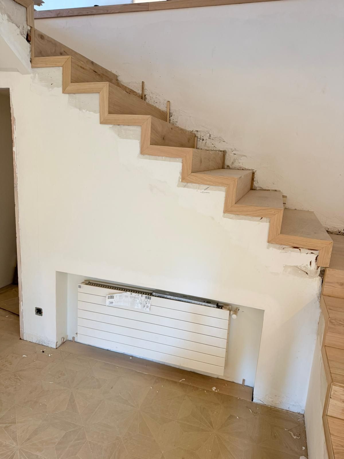 Una escalera de madera sin terminar en una habitación blanca con un radiador 