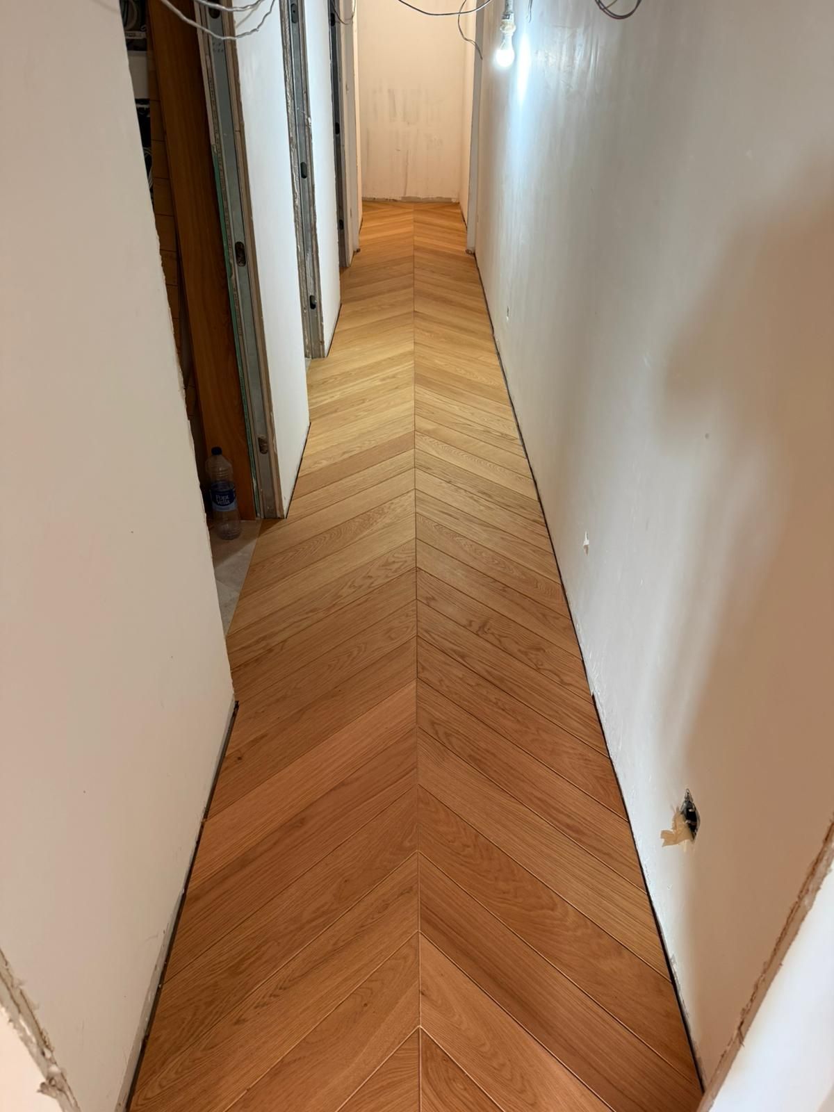 Un pasillo con piso de madera de color marrón claro dispuesto en patrón de chevron