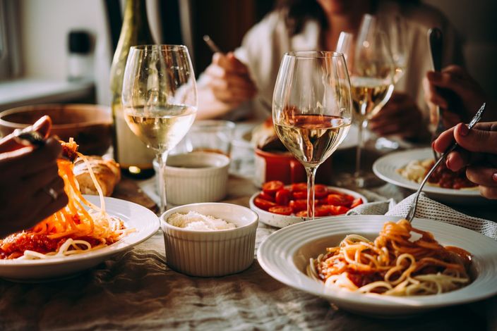 Un grupo de personas está sentada en una mesa comiendo espaguetis y bebiendo vino.