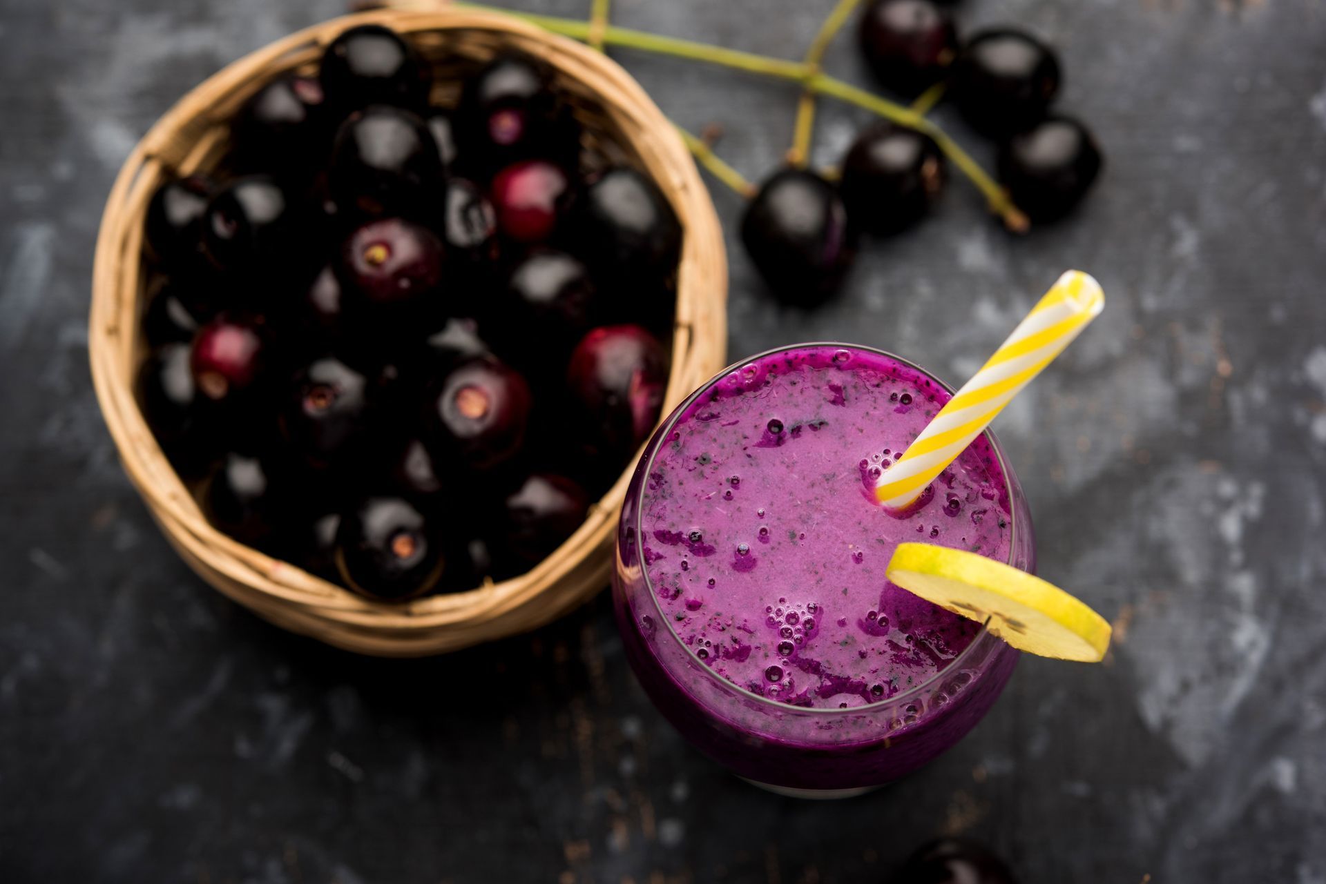 Un batido morado con pajitas junto a un bol de cerezas.