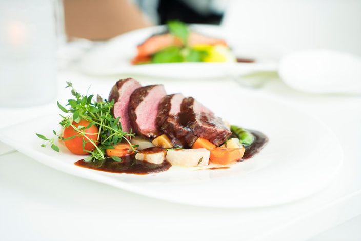 Un plato blanco cubierto con carne y verduras sobre una mesa.