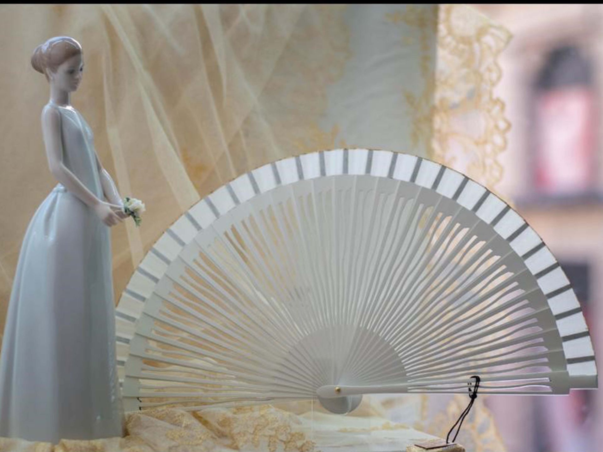 Una estatua de una mujer con un vestido blanco de pie junto a un abanico blanco.