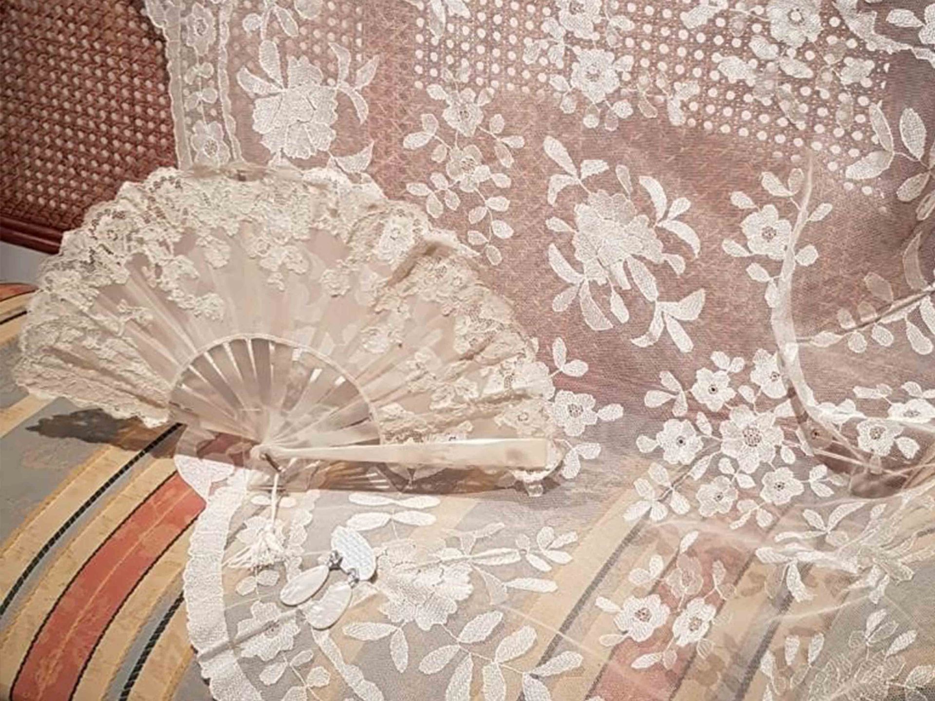 Un abanico de encaje blanco está sentado encima de un sofá a rayas.