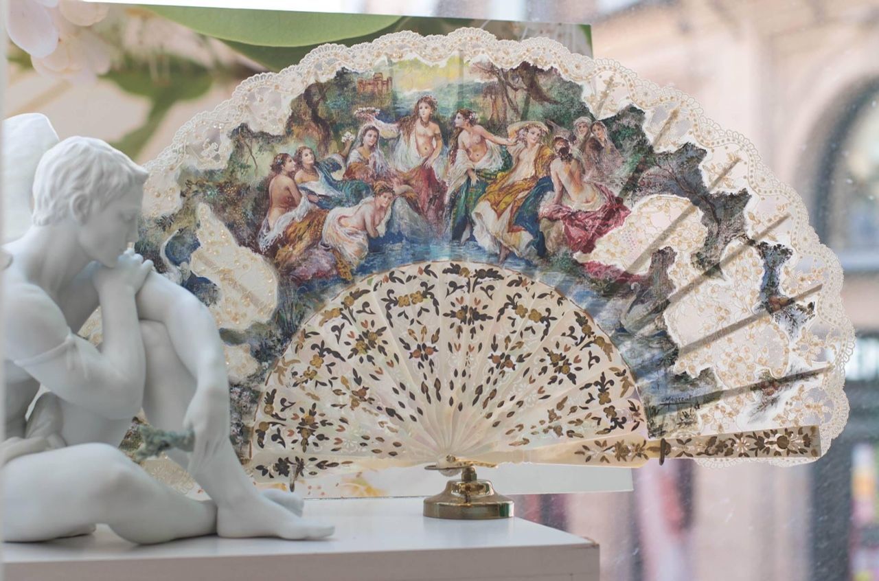 Un abanico con una pintura está sobre una mesa al lado de una estatua.