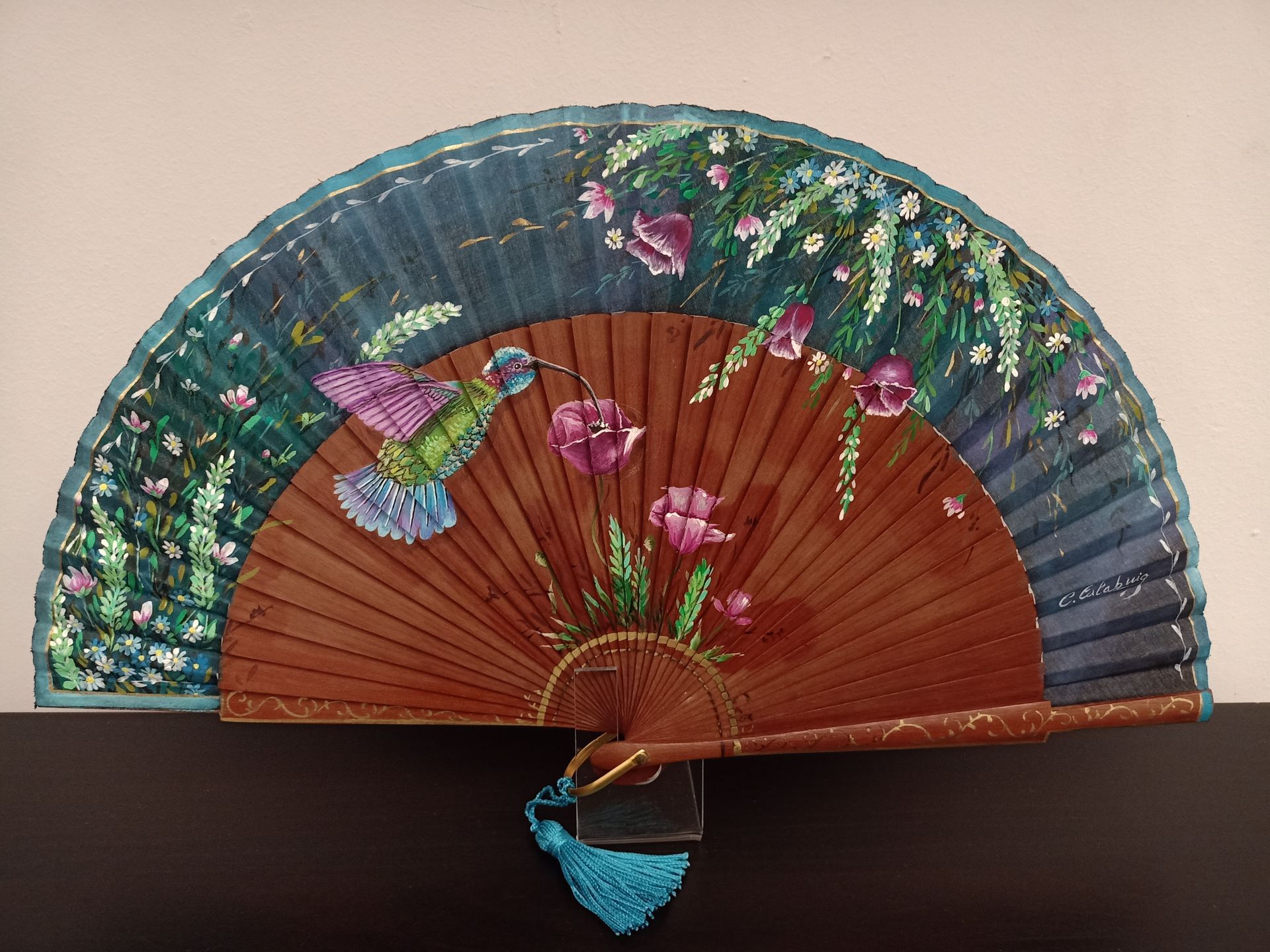 Un abanico con flores y un colibrí pintado en él.