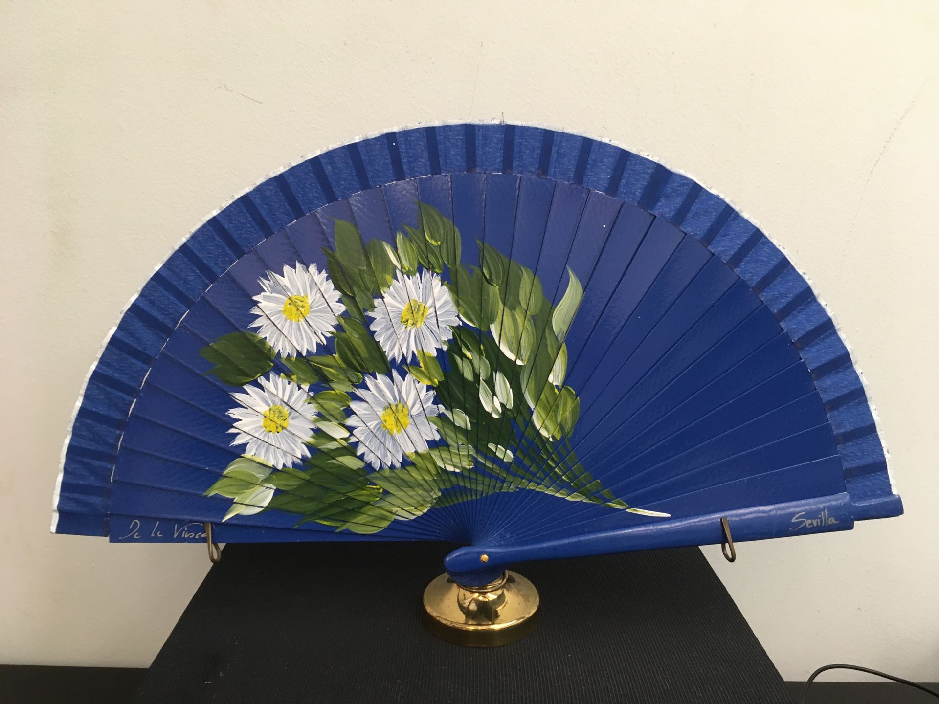 Un abanico azul con margaritas blancas pintadas.