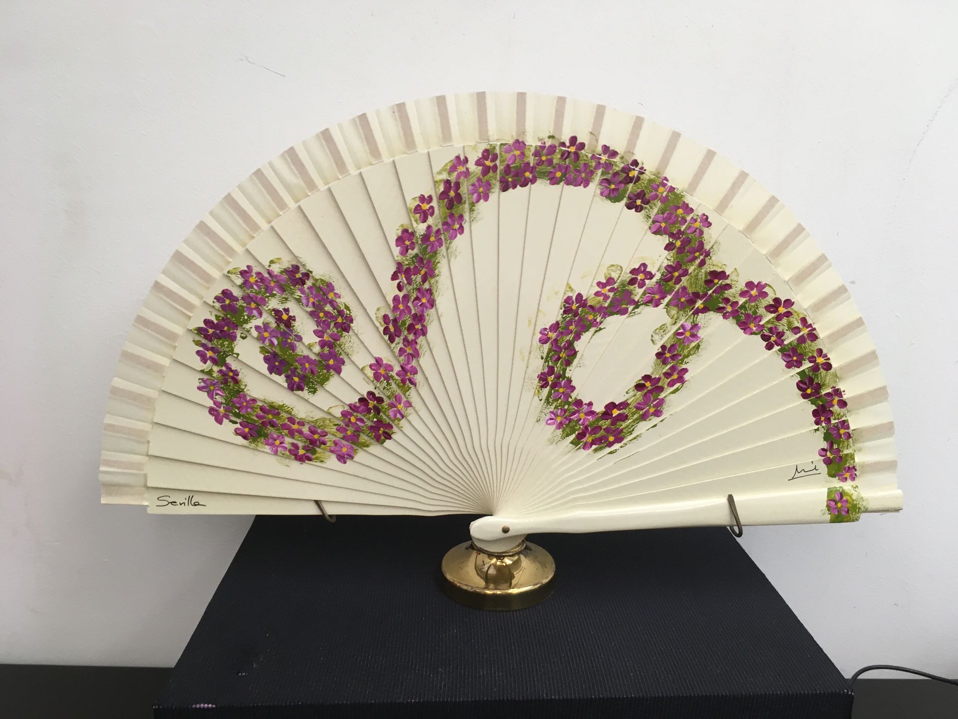 Un abanico blanco con flores de color púrpura está sobre una mesa.