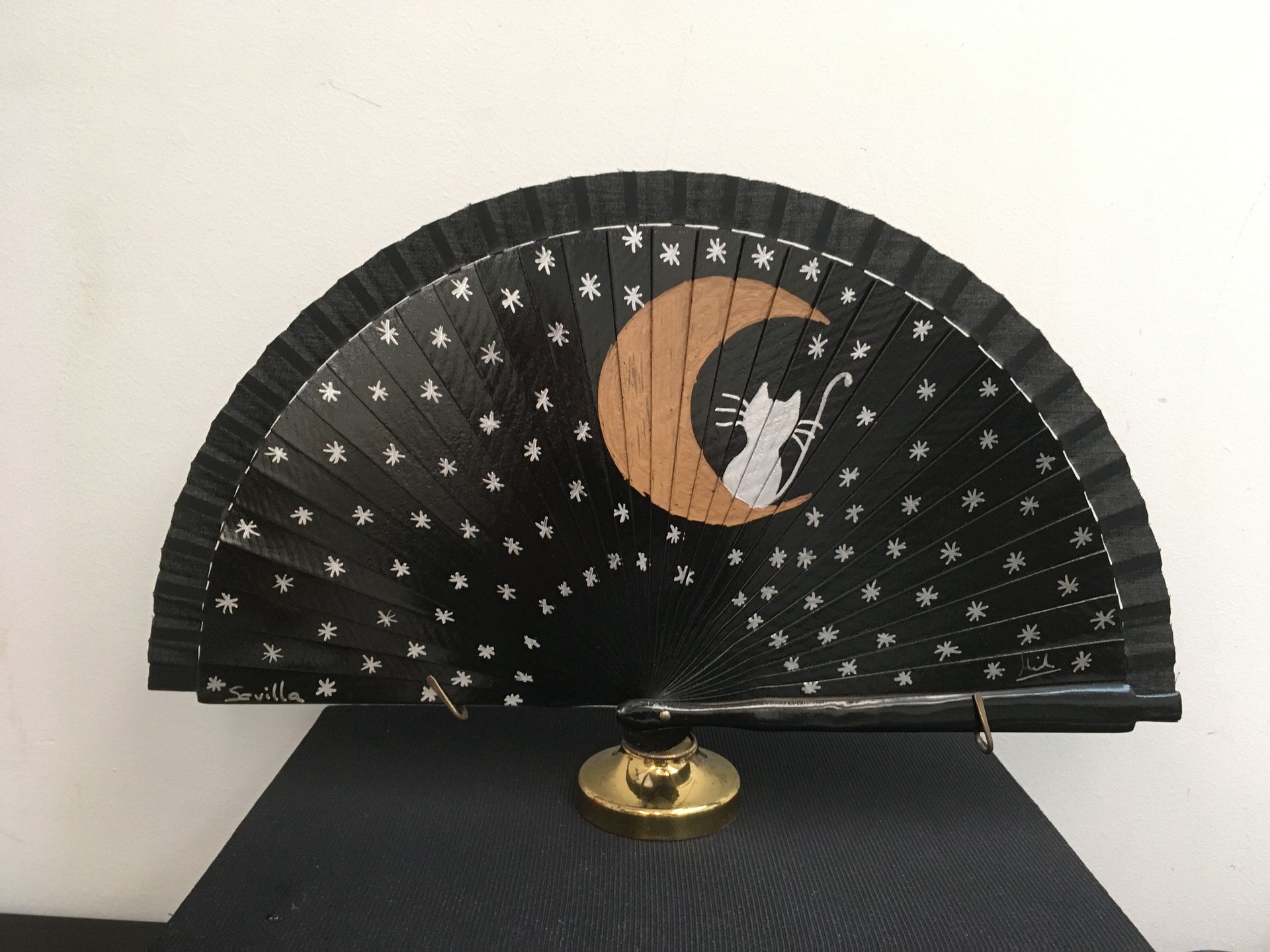 Un abanico negro con un gato y una luna creciente.