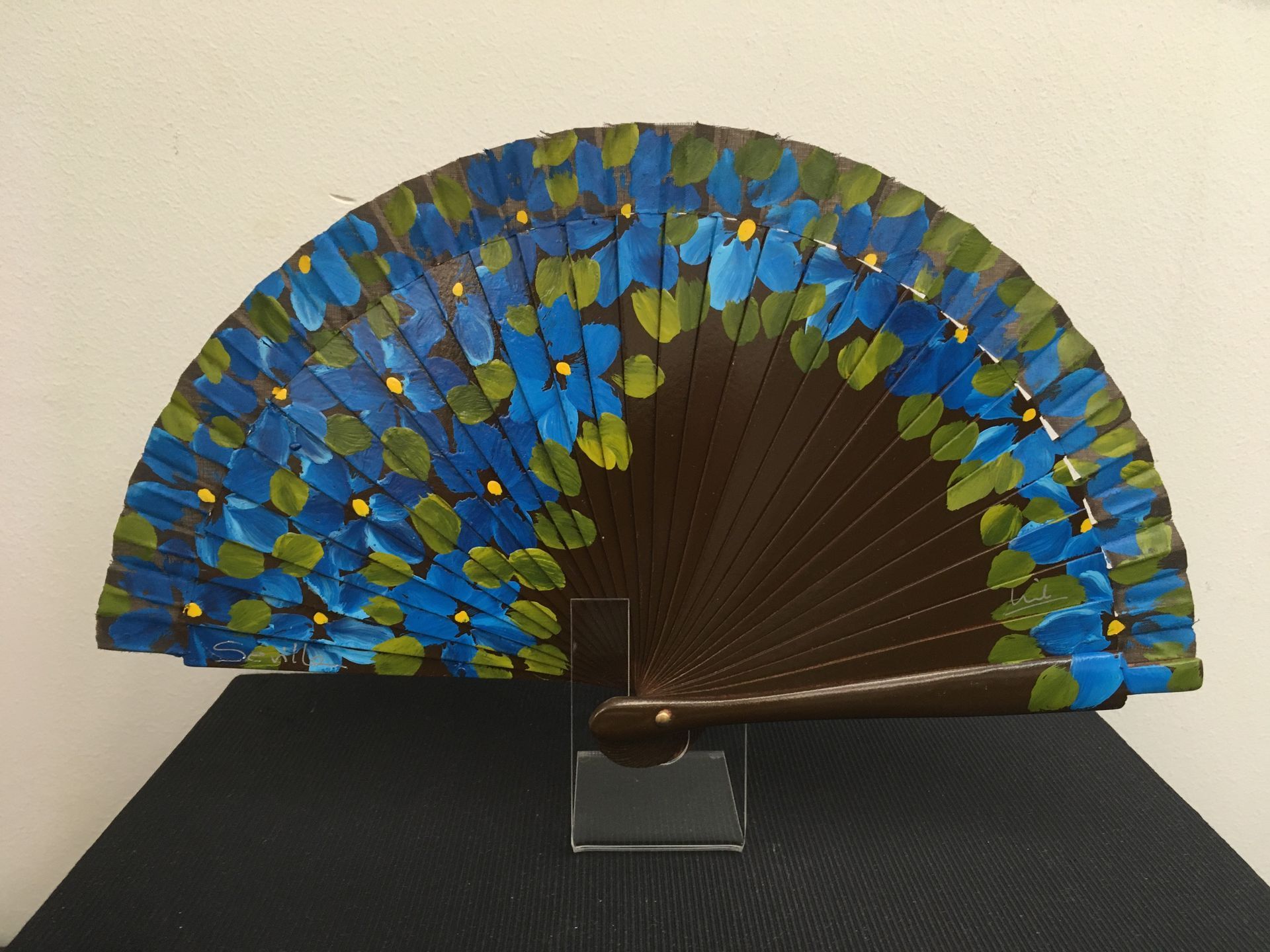 Un abanico con flores azules y verdes pintadas.