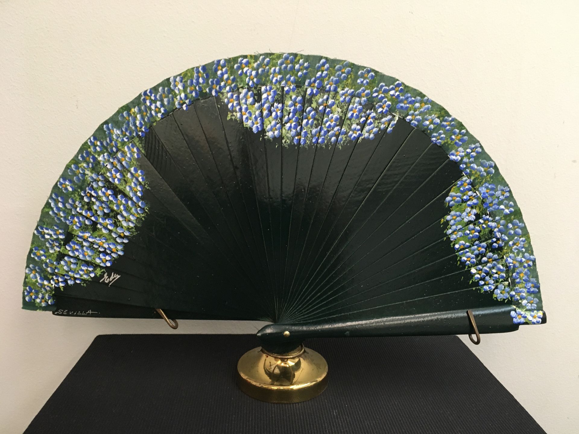 Un abanico negro con flores azules está sobre una mesa.