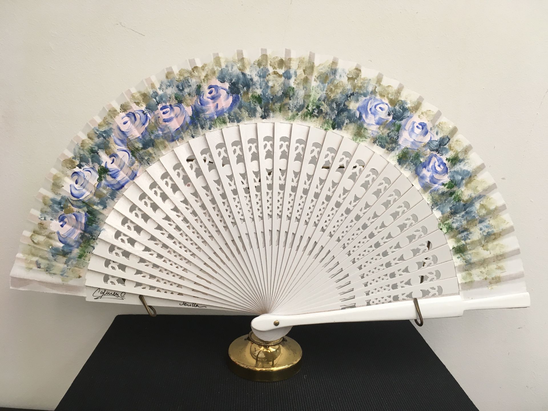 Un abanico blanco con flores azules está sobre una mesa.