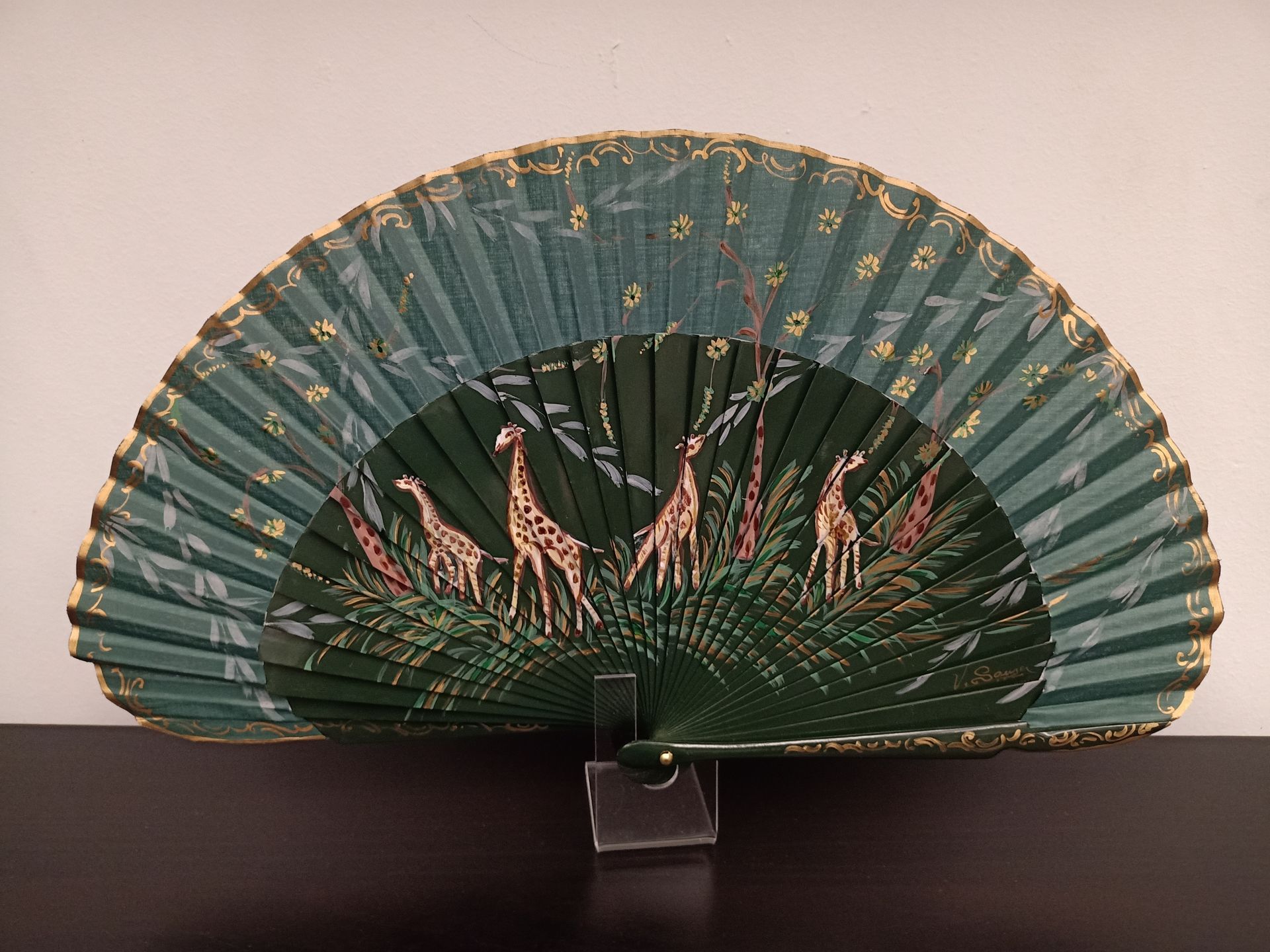 Un abanico verde con jirafas está sobre una mesa.