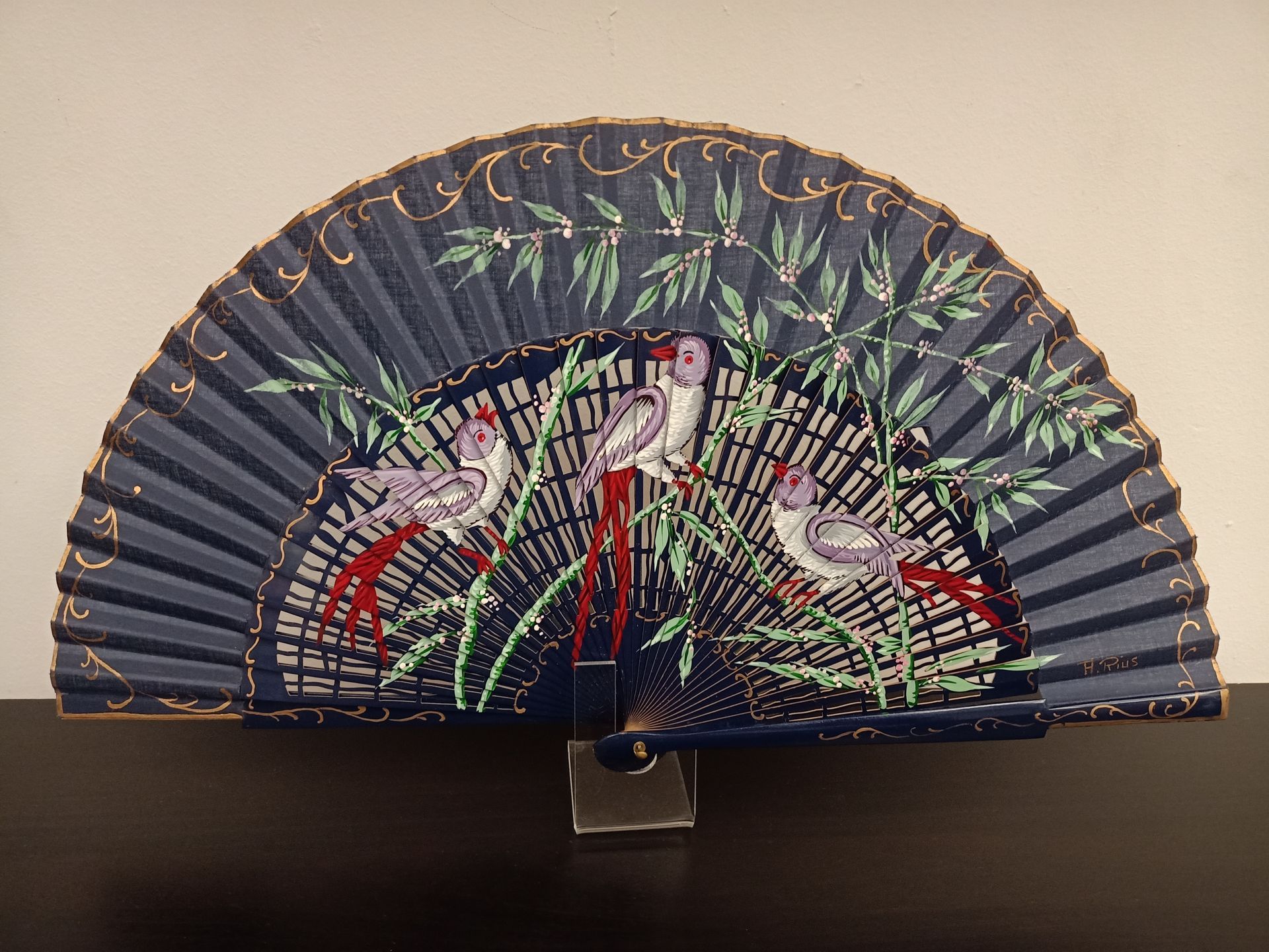 Un abanico azul con pájaros y hojas.