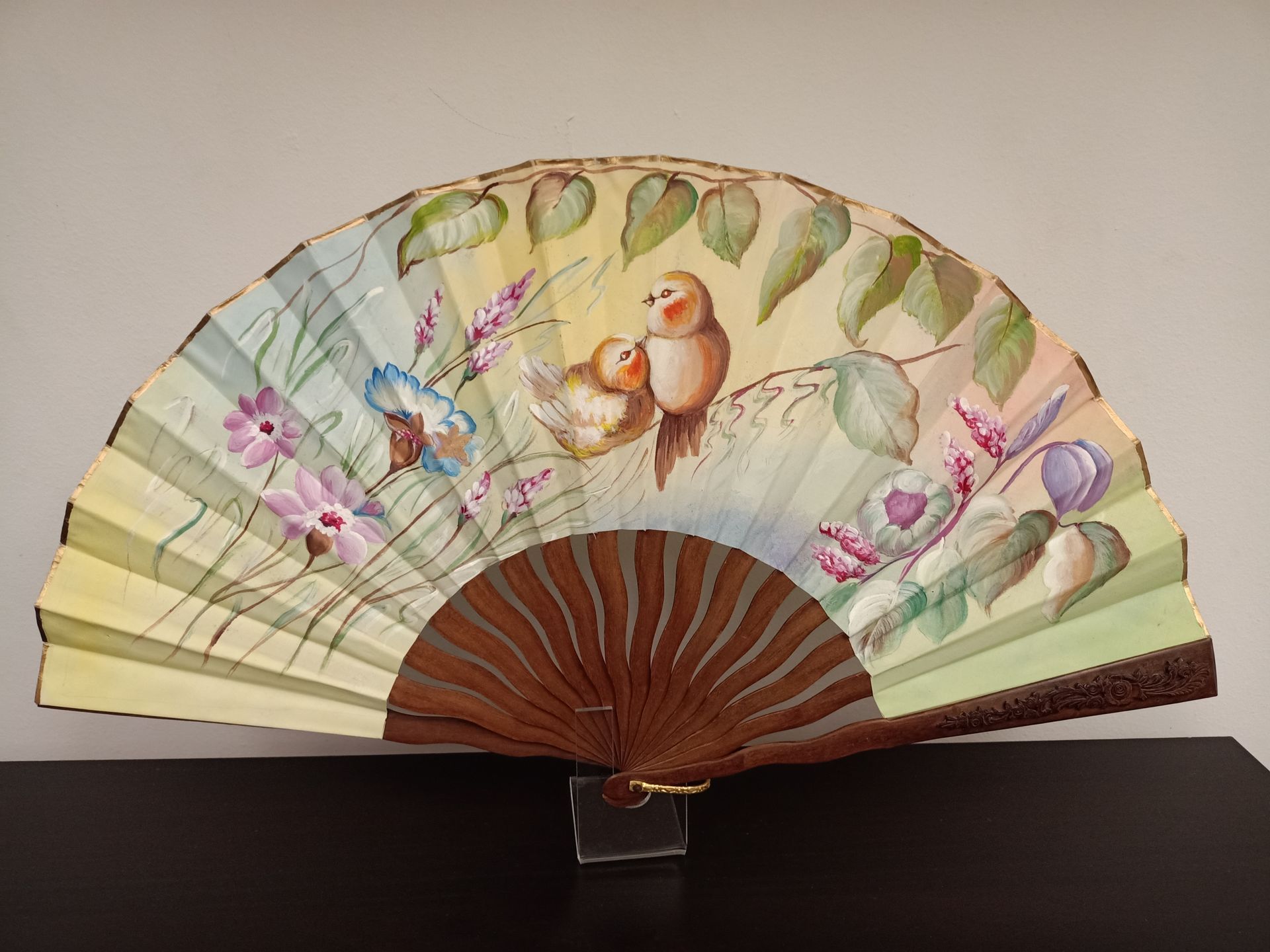 Un abanico con pájaros y flores pintados.