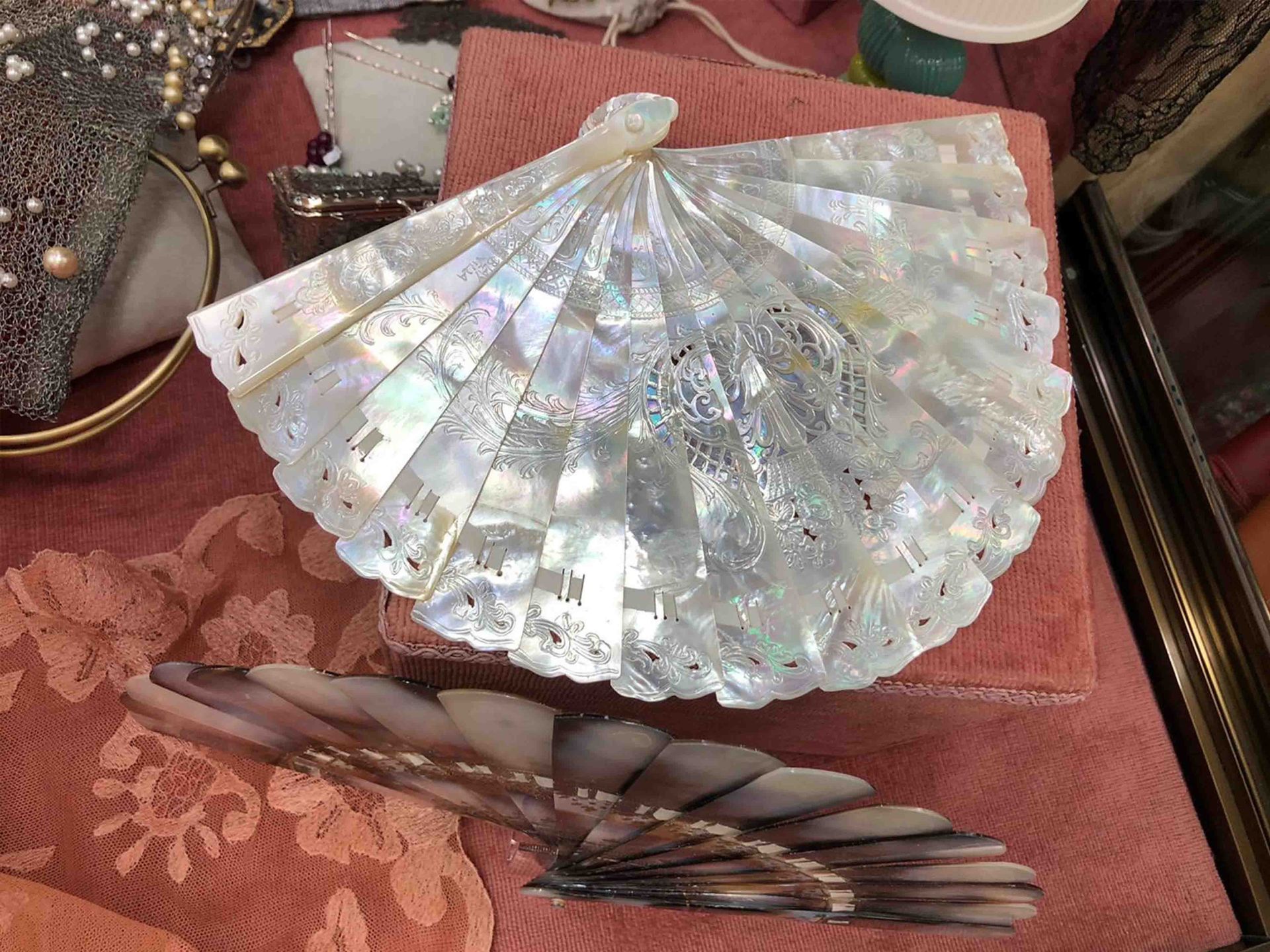 Un abanico blanco reposa sobre un paño rosa sobre una mesa.