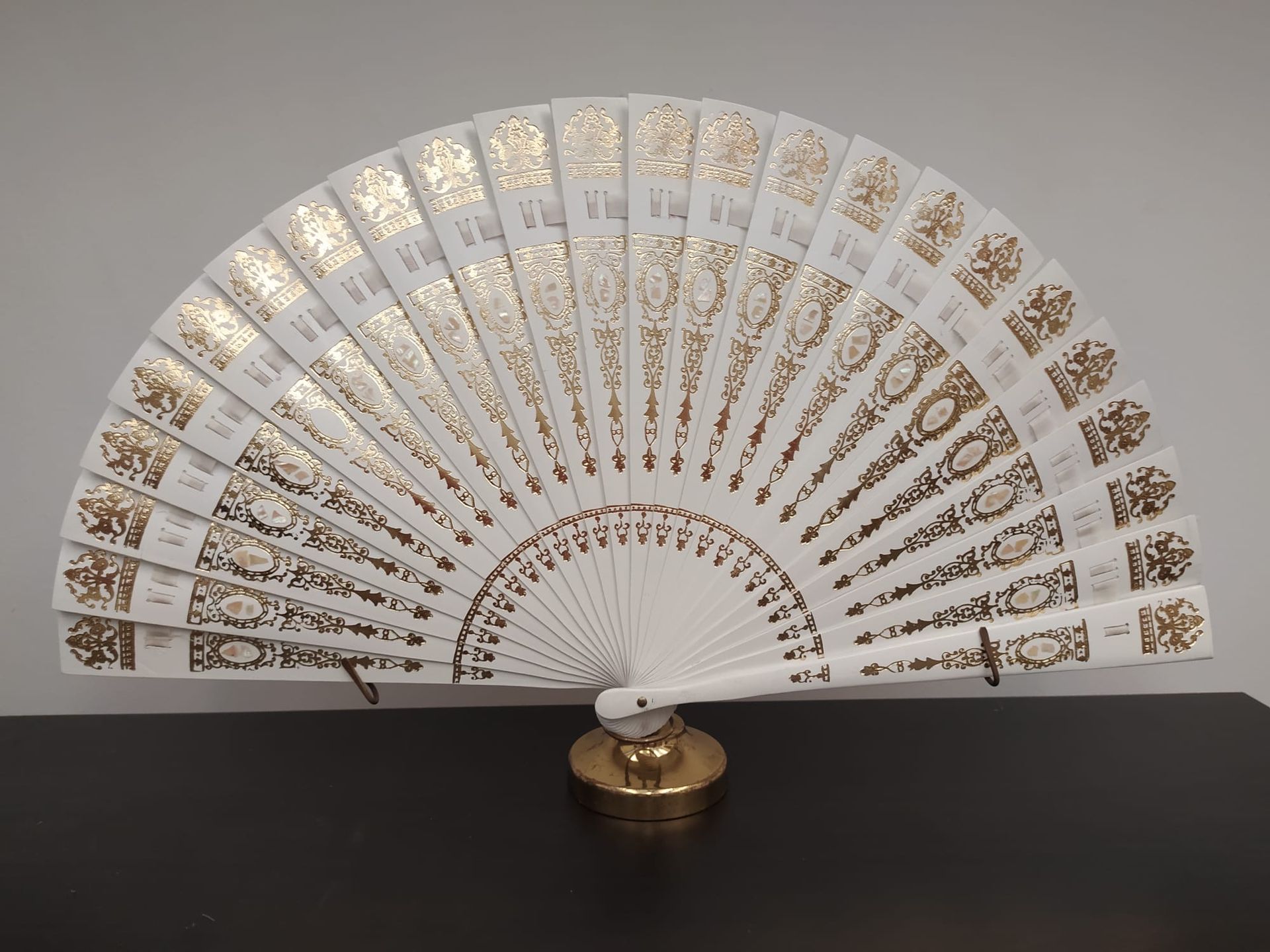 Un abanico blanco y dorado está sobre una mesa.