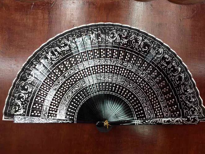 Un abanico negro y plateado está sobre una mesa de madera.