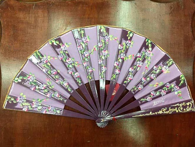 Un abanico morado con flores está sobre una mesa de madera.