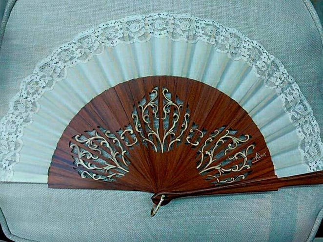 Un abanico de madera con encaje blanco está sobre una silla.