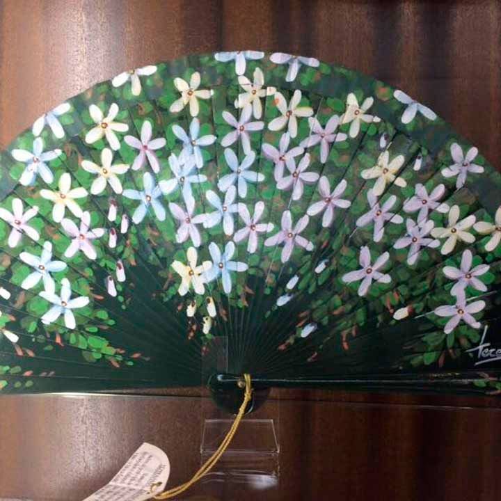 Un abanico verde con flores blancas pintadas.