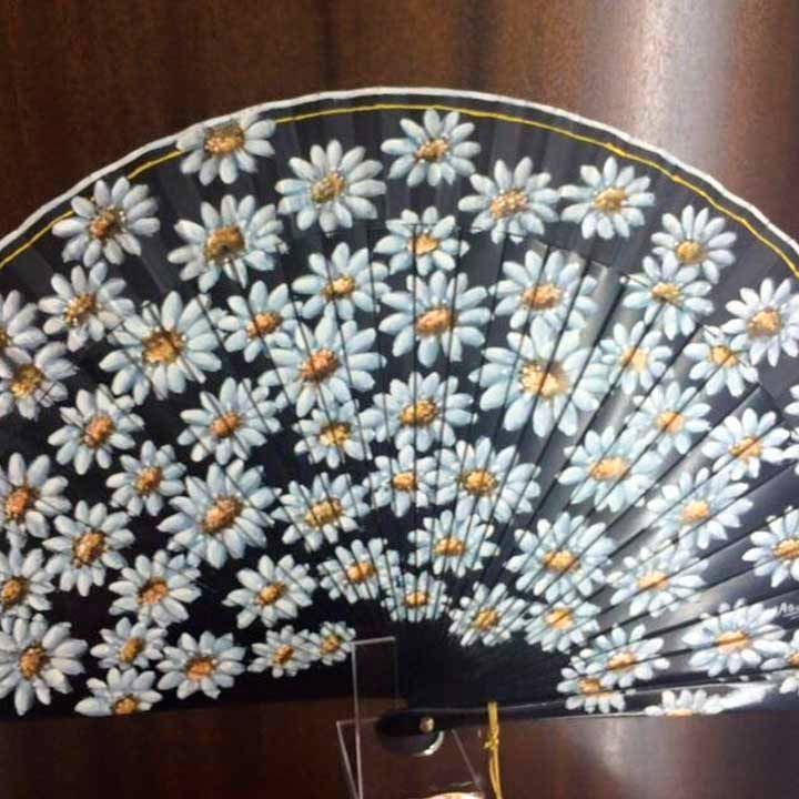 Un abanico negro con margaritas blancas pintadas.