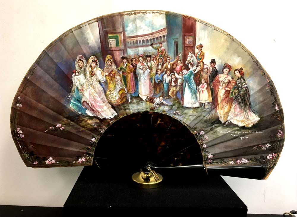 Un abanico con una pintura está sobre una mesa.