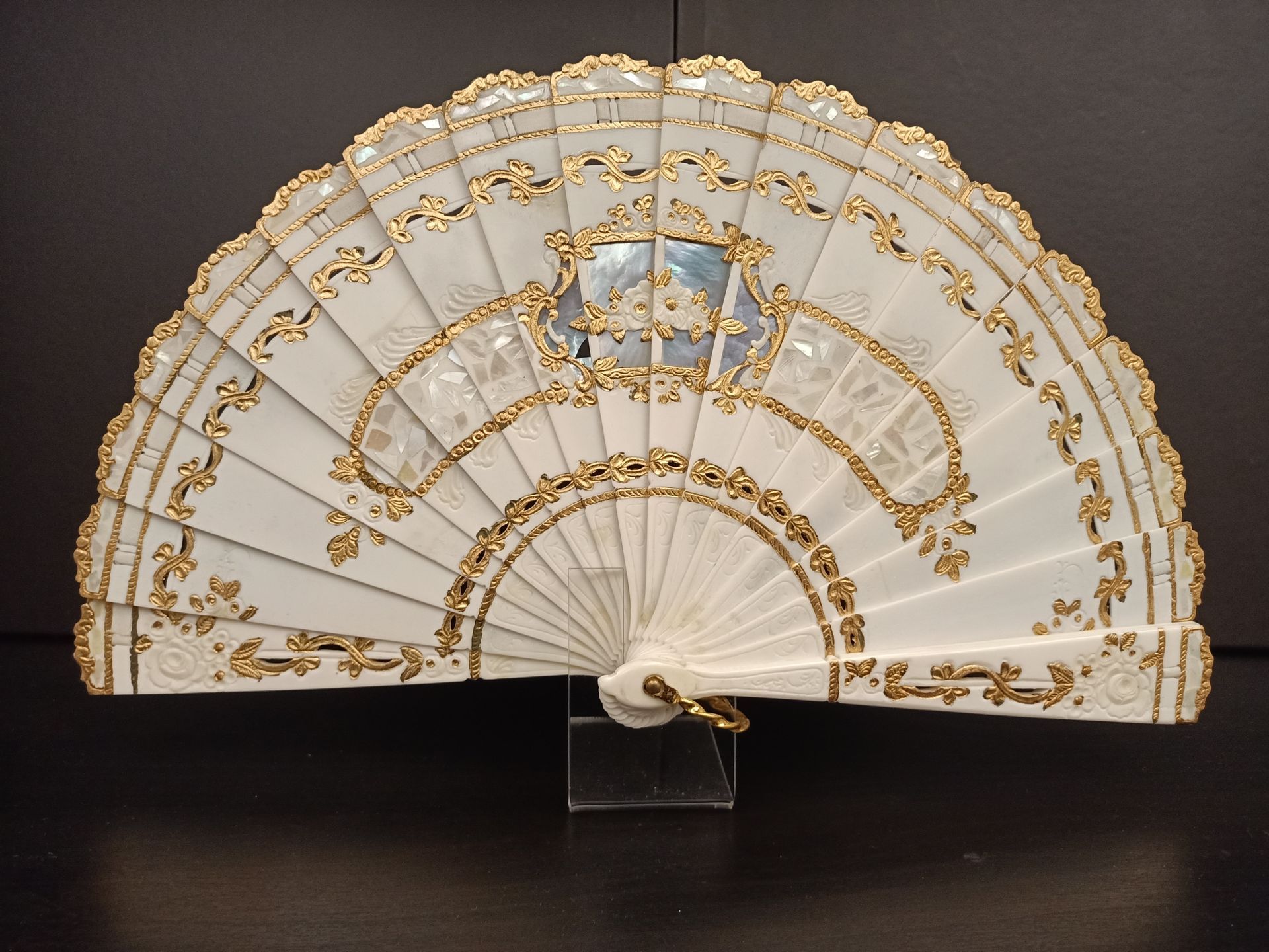 Un abanico blanco con ribete dorado reposa sobre una mesa.