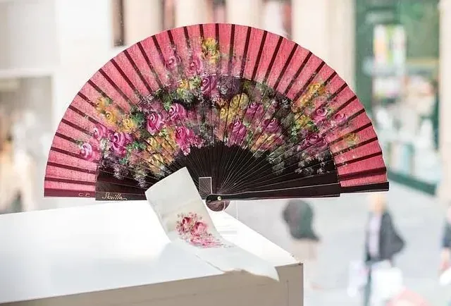 Un abanico rosa con flores está sobre una mesa.