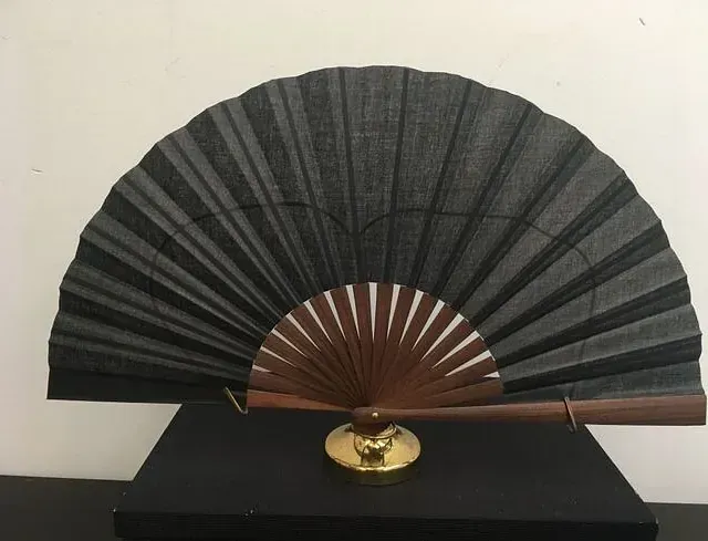 Un abanico negro con mango de madera está sobre una mesa negra.
