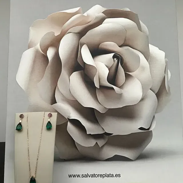 Un conjunto de collar y aretes se exhibe frente a una gran rosa de papel.