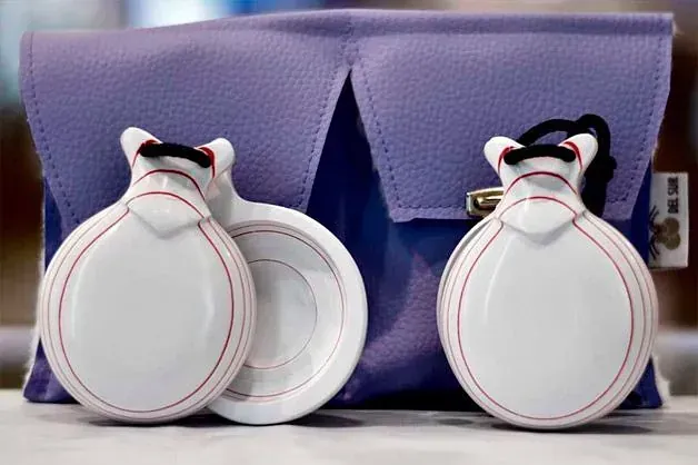 Un par de castañuelas blancas sobre una bolsa morada.