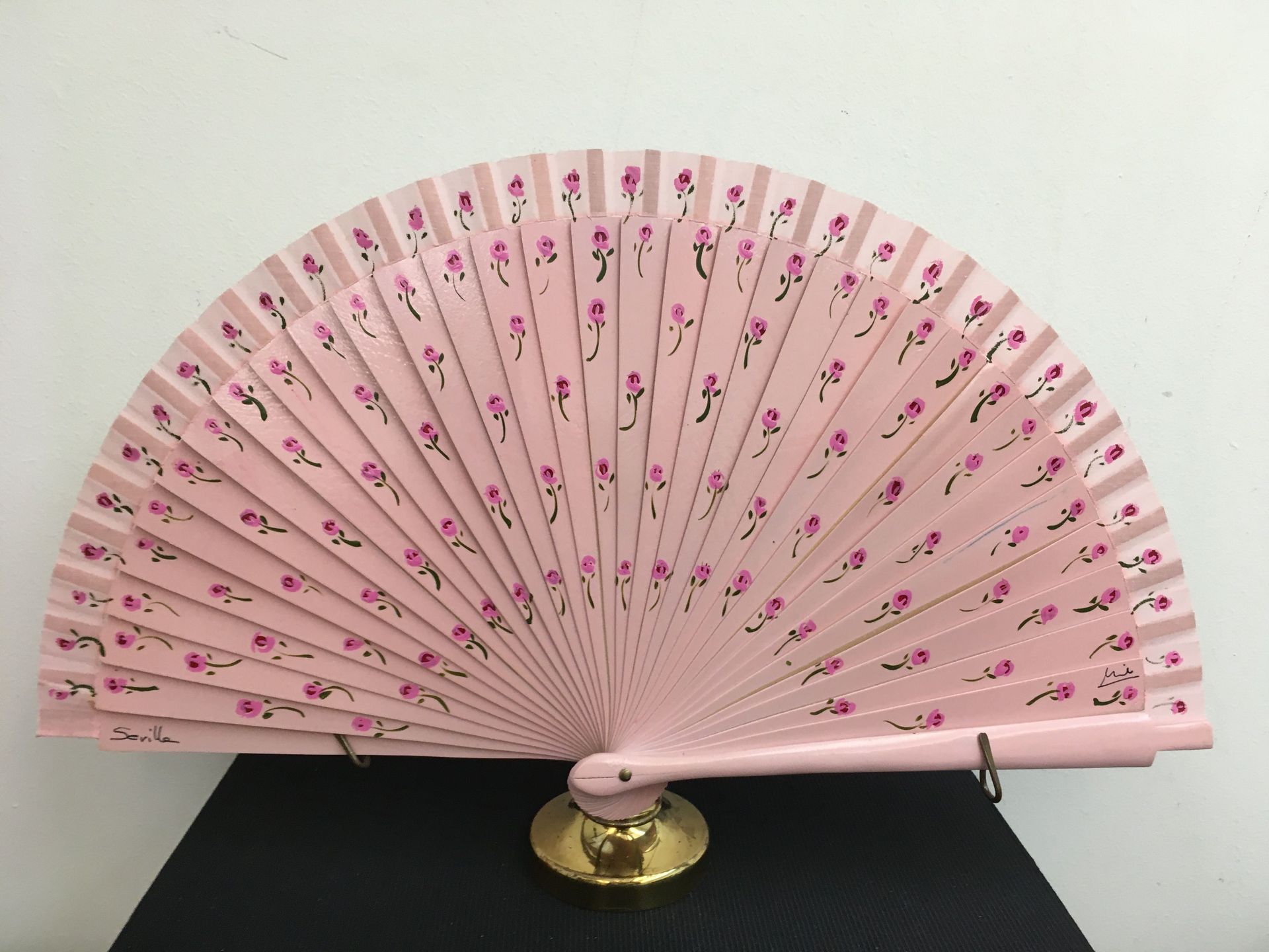Un abanico rosa con flores rosas está sobre una mesa.